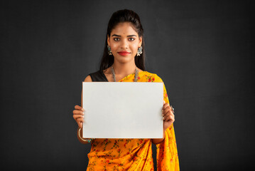 Wall Mural - A young girl or businesswoman wearing a saree and holding a signboard in her hands on a gray background.