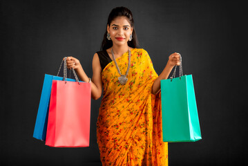 Sticker - Beautiful Indian young girl holding and posing with shopping bags on a grey background