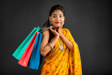 Sticker - Beautiful Indian young girl holding and posing with shopping bags on a grey background