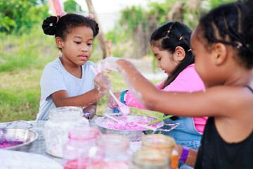 Wall Mural - Lovely Asian and African girls making and play colorful dough together at playground, summer camp learning