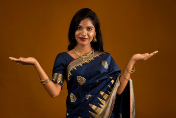 Sticker - Portrait of Indian traditional young woman or girl presenting something, showing copy space on her palm on a brown background