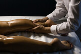 Fototapeta  - Uma terapeuta vestido de branco, fazendo massagem na perna de paciente deitado em maca, com o uso de óleo terapêutico.