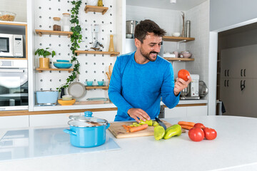 Wall Mural - Young sporty man cutting and cooking fresh natural vegetables at kitchen and cooking for healthy lunch. Self care yoga nutritionist having healthy meal after workout.