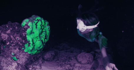 Sticker - Night snorkeling. Woman swims underwater at night and watches coral reef shining acid green in ultraviolet light