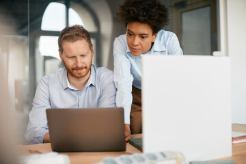 multiracial entrepreneurs cooperate while working on laptop in office.