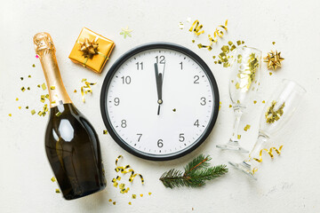 New year celebration concept with a bottle of champagne and two glasses toasting. Christmas gift box, alarm clock and fir tree branch on colored table. Top view Copy space