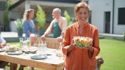 Wall Mural - Happy senior woman serving salad at multi generation garden party in summer.