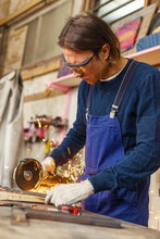 Side View Of Young Metalworker In Protective Eyewear Cutting Piece Of Metal With Angle Grinder Standing At Workbench In Workshop