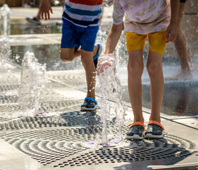 Wall Mural - Boy having fun in water fountains. Child playing with a city fountain on hot summer day. Happy kids having fun in fountain. Summer weather. Active leisure, lifestyle and vacation