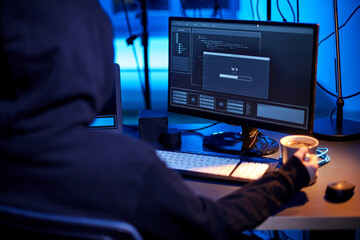 cybercrime, hacking and technology concept - close up of hacker in dark room drinking coffee and using computer virus program for cyber attack