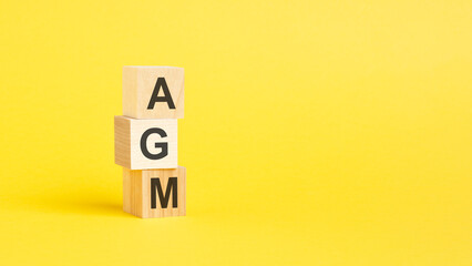 Poster - AGM - Annual General Meeting - text on wooden block with yellow backgrounds.