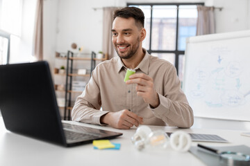 Wall Mural - distance education, school and green energy concept - happy smiling male teacher with laptop computer and alkaline battery having online class at home office