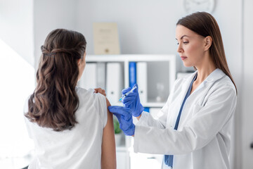 Wall Mural - health, medicine and pandemic concept - female doctor or nurse wearing protective medical gloves with syringe vaccinating patient at hospital