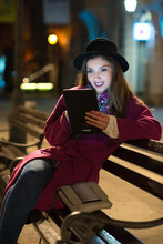 Young Woman Sitting On The Bench At Night And Using Tablet