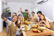 © CandyRetriever  - Group of Cheerful Asian man and woman friends enjoy dinner party using mobile phone taking selfie together at home. Happy male and female reunion meeting and celebrating on holiday event vacation.