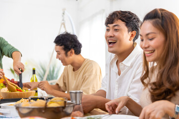 Wall Mural - Group of Asian man and woman friends having dinner with drinking wine and talking together on dining table at home. Happy people friendship enjoy reunion meeting celebration party on holiday vacation