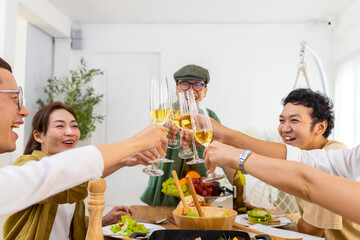 Wall Mural - Group of Cheerful Asian man and woman friends toasting wine glasses while having dinner together at home. Happy male and female reunion meeting event celebrating party on holiday vacation