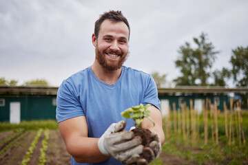 Wall Mural - Happy farming worker with a plant on an agriculture farm with a smile. Farmer advertising sustainability, growth and ecology on a green field or land in a nature eco friendly environment countryside