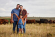 © Nina Lawrenson/peopleimages.com - Happy family standing on a farm, cow in background and with a vision for growth in industry portrait. Countryside couple, people or farmer in a field of grass, cattle and free range livestock animals