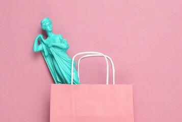 Paper shopping bag with antique statue on a pink background. Minimalism. Flat lay