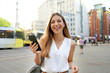 Attractive business woman holding smartphone looking at camera on urban background. Waist-up shot.