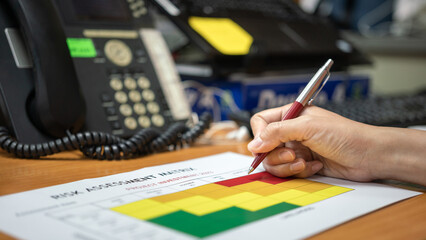 Wall Mural - action of a manager is using ballpoint pen to evaluate on risk assessment matrix of the project inve