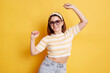 © sementsova321 - Indoor shot of attractive extremely happy woman wearing striped t shirt and jeans, raised arms and dancing, having good news and high spirit, posing isolated over yellow background.