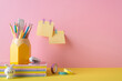 Back to school concept. Photo of school accessories on yellow desk stand for pens bunny shaped sharpener stapler stack of colorful copybooks adhesive tape and sticky note paper attached to pink wall