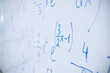 Physical and mathematical formulas written with a blue marker on a white board in a high school classroom. Abstract background close-up