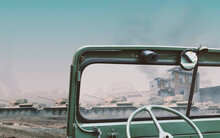 Interior Of A Vintage Green Convertible Military 4x4 SUV Car Dashboard With A War Scene Of Tanks And Burning Houses Visible Off Focus Through The Windshield With Copy Space