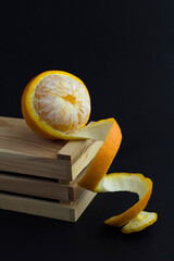 Wall Mural - Close-up on peeled orange on the wooden box  the black background. Copy space. Location vertical.