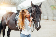 Beautiful Blond Professional Female Jockey Standing Near Horse. Woman Horse Rider Is Preparing To Equitation. Girl And Horse. Equestrian Sport Concept. Riding Vacation.friendship With Horse.copy Space