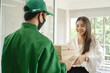Young Asian woman picked up the package from delivery man rider ware green uniform with smile feeling happy. pay by cash. online shopping and food delivery concept