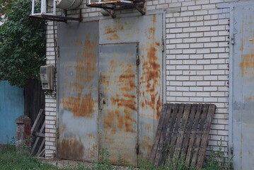 Canvas Print - white brick facade of an old garage with a gray metal closed gate in brown rust on the street