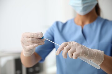 Doctor holding buccal cotton swab and tube for DNA test in clinic, closeup