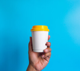 Wall Mural - Man hand holding a white coffee cup peper, filled with hot black coffee(americano), no sugar no milk, ready to drink, refreshing. aroma awake fresh to work placed on a blue isolated background
