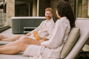 Young couple relaxing on beds and drinking fresh orange juice on the outdoor terrace