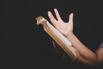 Canvas Print - Close up of christian woman hand holding holy bible pray and worship for thank god in church with black background, adult female person are reading book,