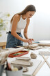 © ninelutsk - Woman rolling clay, making ceramic plate in studio with floral pattern. Handmade creative work. Pottery workshop for adults.