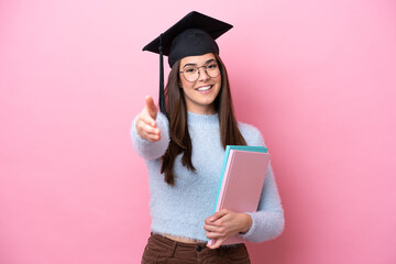 Wall Mural - Young student Brazilian woman wearing graduated hat isolated on pink background shaking hands for closing a good deal