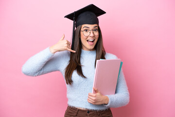 Wall Mural - Young student Brazilian woman wearing graduated hat isolated on pink background making phone gesture. Call me back sign