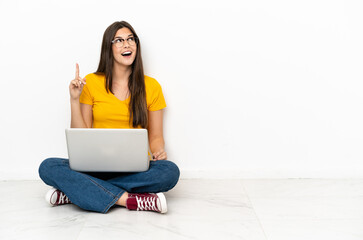 Wall Mural - Young woman with a laptop sitting on the floor intending to realizes the solution while lifting a finger up