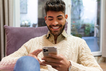 Happy Young Ethnic Man Messaging On Smartphone At Home