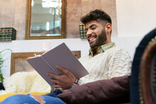 Positive Young Hispanic Guy Reading Interesting Book At Home