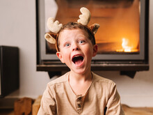 Amazed Boy In Reindeer Antlers Near Fireplace
