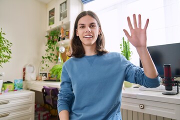 Handsome teenage male waving hand looking at webcam