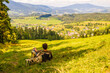 Młody mężczyzna z plecakiem siedzący na skraju lasu patrzący na piękny krajobraz w górach