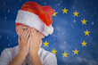 A energy crisis in the Europe.A boy wearing a Santa hat is sad due to the gas crisis in Europe.The child is cold without outerwear clothes on the background of the eu flag.Copy space.Closeup.