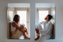 Dreamy couple sitting on windowsills and looking out window