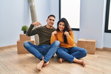 Sticker - Young couple sitting on the floor at new home looking confident with smile on face, pointing oneself with fingers proud and happy.